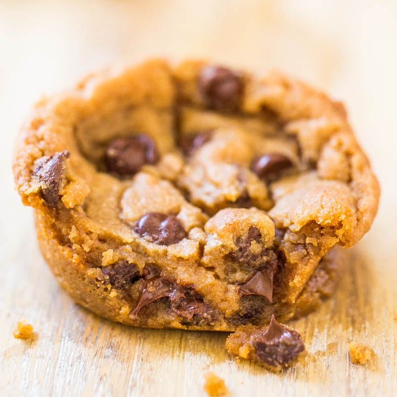 A close-up of a chocolate chip cookie with melted chocolate chips on a wooden surface.