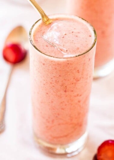 A smoothie in a glass with a spoon on the side.
