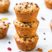 Three chocolate chip muffins stacked on top of each other on a white wooden surface.