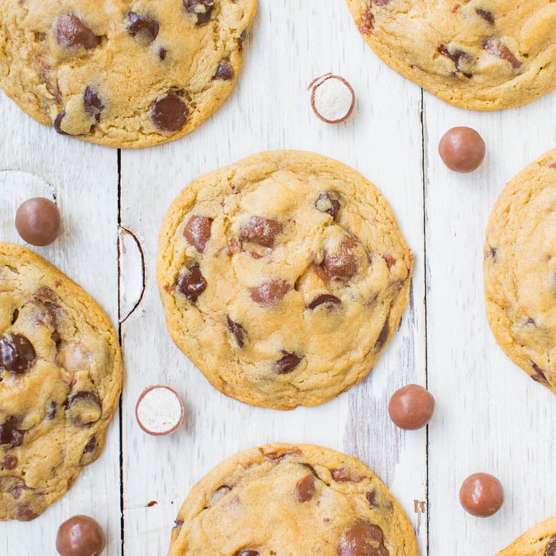 Freshly baked chocolate chip cookies with scattered candies on a wooden surface.