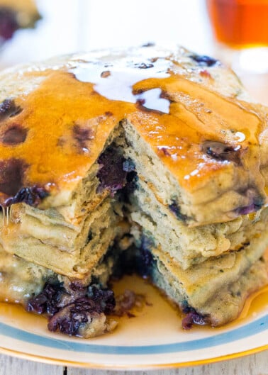 A stack of blueberry pancakes with syrup on a plate.