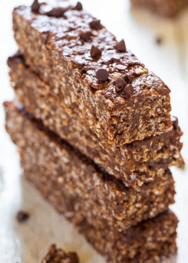 Three chocolate oat bars stacked on a wooden table, sprinkled with mini chocolate chips.