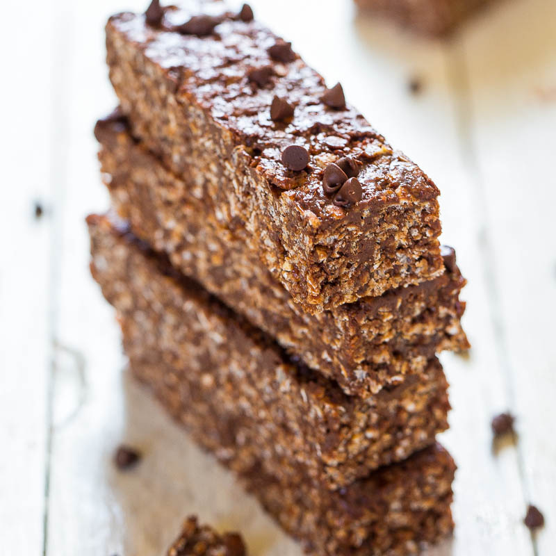 Three chocolate oat bars stacked on a wooden table, sprinkled with mini chocolate chips.