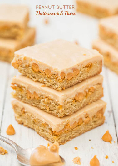 Homemade peanut butter butterscotch bars stacked on a white surface with a spoon of butterscotch sauce.