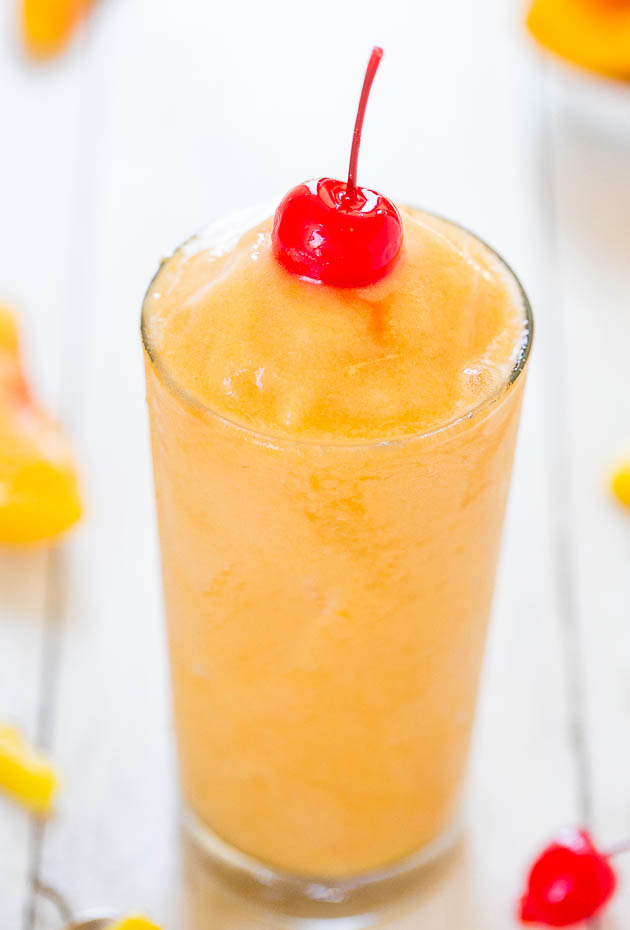 Tropical alcoholic slushie in a tall glass garnished with a maraschino cherry
