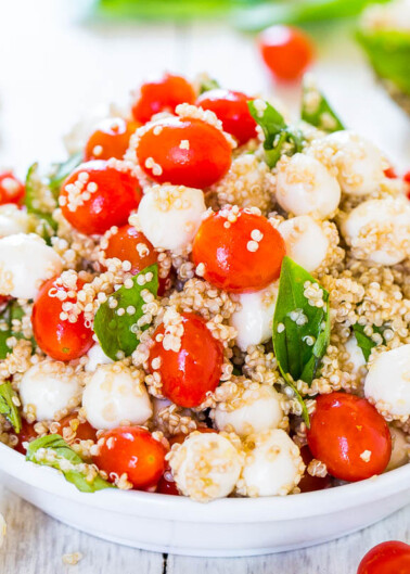 A bowl of quinoa salad with cherry tomatoes, spinach, and mozzarella cheese.