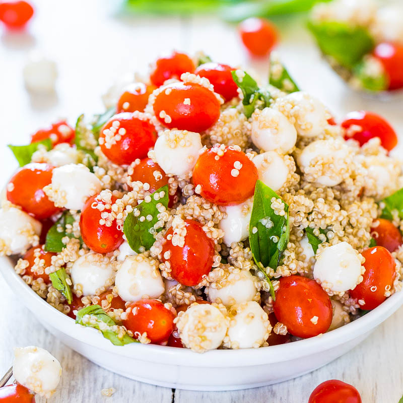 A bowl of quinoa salad with cherry tomatoes, spinach, and mozzarella cheese.
