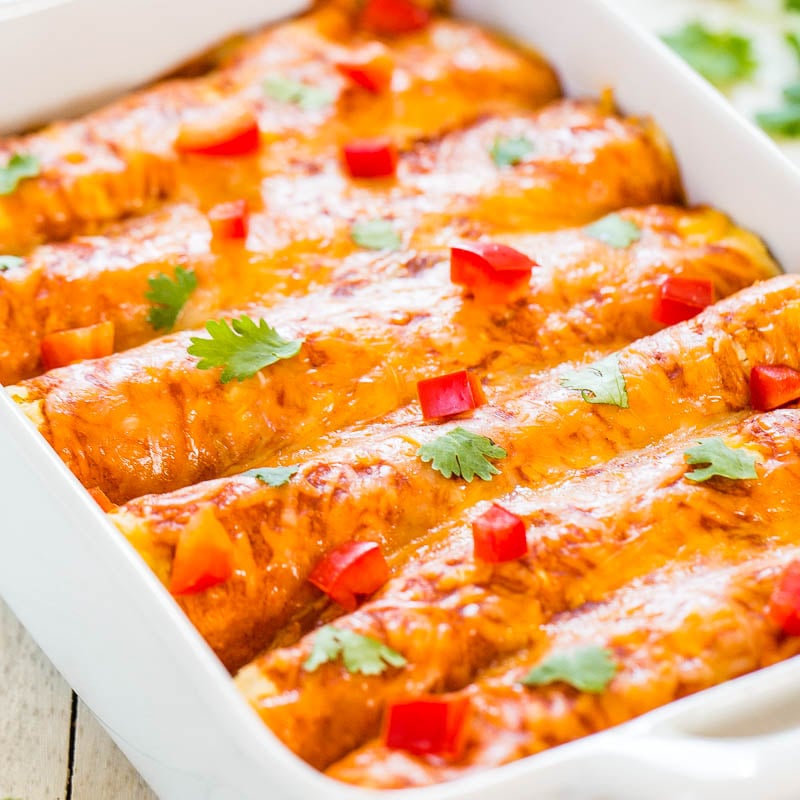 A baking dish containing enchiladas topped with melted cheese and garnished with diced red peppers and cilantro.