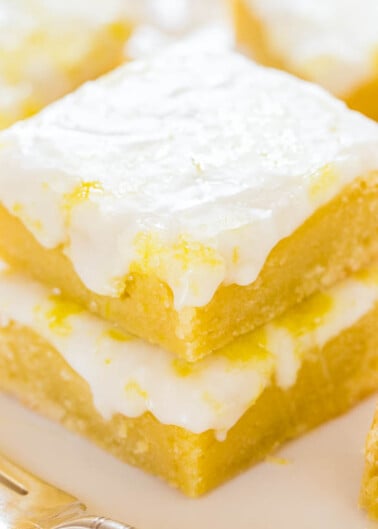 A close-up of a lemon bar with a dusting of powdered sugar on a plate.