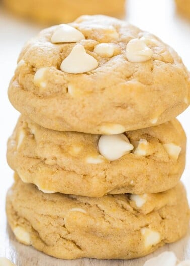 A stack of white chocolate chip cookies on a light wooden surface.