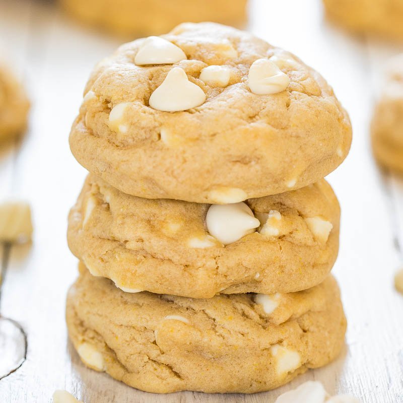 A stack of white chocolate chip cookies on a light wooden surface.