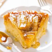 A slice of caramel-drizzled cake on a white plate with a spoon.