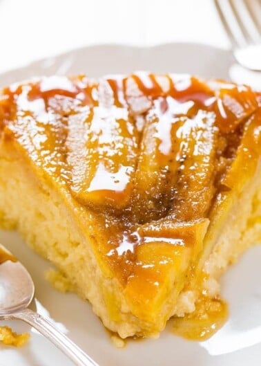 A slice of caramel-drizzled cake on a white plate with a spoon.