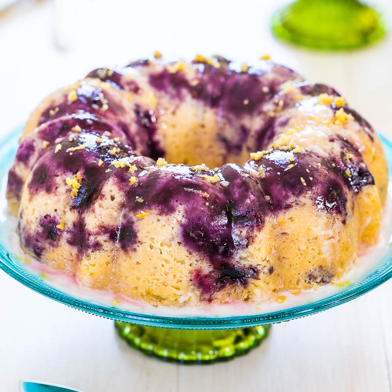 A brightly colored blueberry lemon bundt cake on a glass stand.