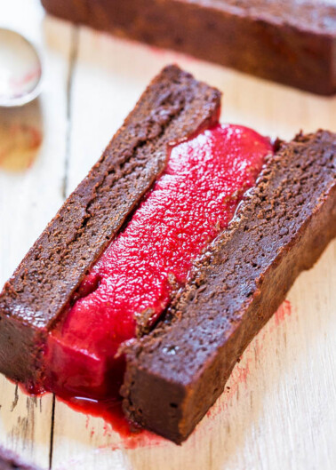 A chocolate dessert with a bright red jelly filling on a wooden surface.