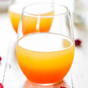 Two glasses of orange-colored beverage on a white wooden surface.