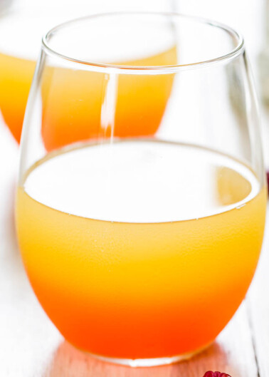 Two glasses of orange-colored beverage on a white wooden surface.