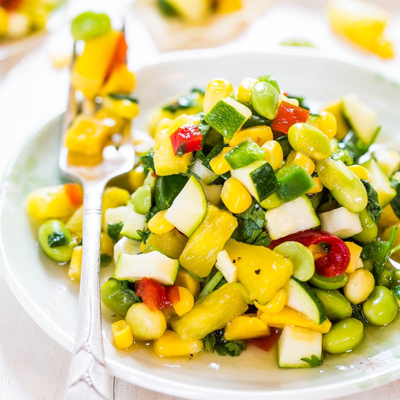 A vibrant bowl of mixed vegetable salad with corn, zucchini, tomatoes, and beans.