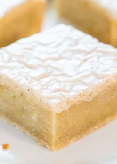 A single square piece of lemon bar dessert with powdered sugar on top, served on a white plate.