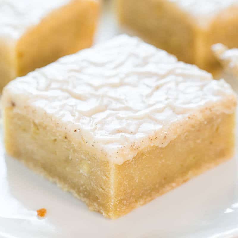 A single square piece of lemon bar dessert with powdered sugar on top, served on a white plate.