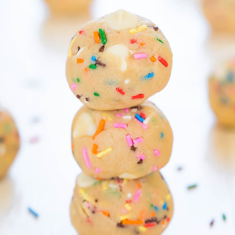 Stack of three sprinkle-covered cookie dough balls on a white background.