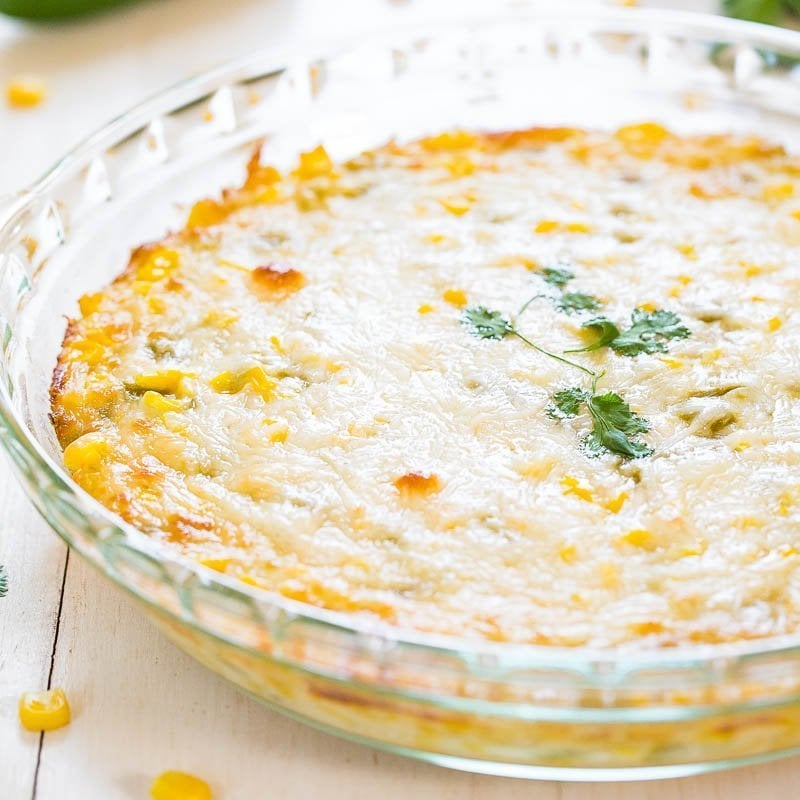 A baked corn casserole topped with melted cheese in a glass dish.