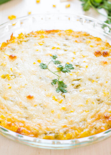 A freshly baked corn casserole topped with melted cheese and garnished with a sprig of parsley, served in a glass dish.