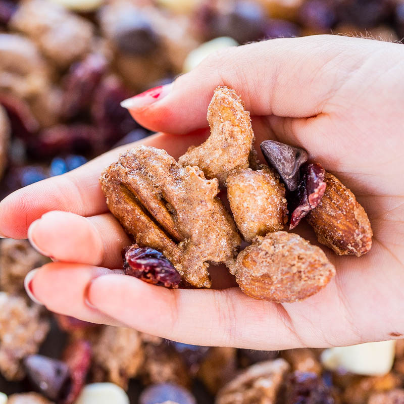 A hand holding a selection of candied nuts and dried berries.