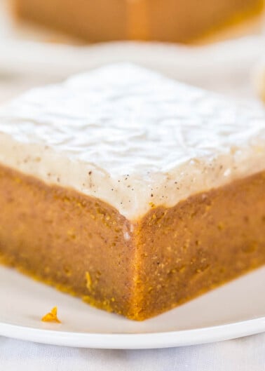 A slice of frosted pumpkin cake on a white plate.