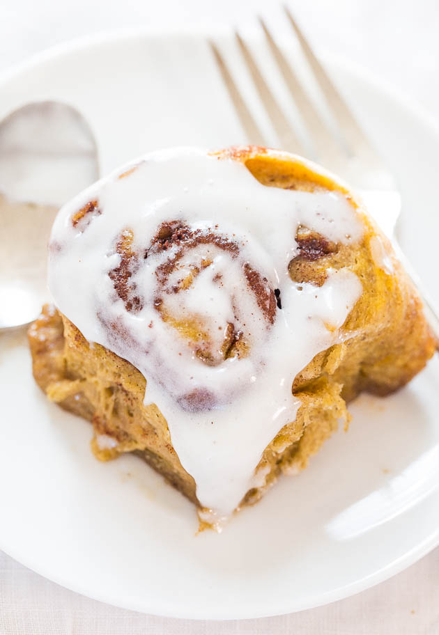 a glazed pumpkin cinnamon roll on a white plate with a fork