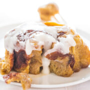 A freshly baked cinnamon roll topped with icing on a white plate.