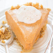 A slice of pumpkin pie topped with whipped cream and a sprinkle of cinnamon on a white plate.