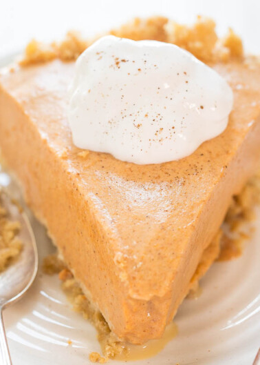 A slice of pumpkin pie topped with whipped cream and a sprinkle of cinnamon on a white plate.
