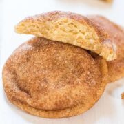 Freshly baked snickerdoodle cookies with one broken in half, showing the soft interior, dusted with cinnamon sugar.