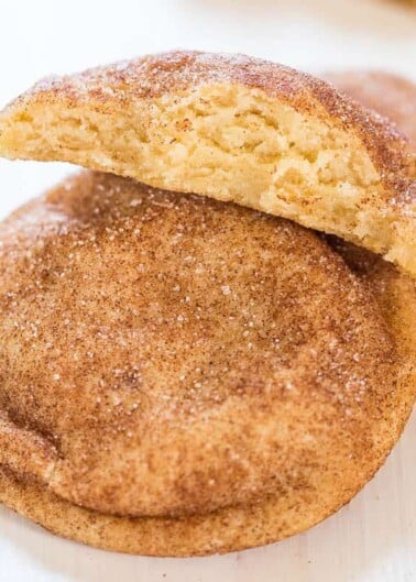 Freshly baked snickerdoodle cookies with one broken in half, showing the soft interior, dusted with cinnamon sugar.