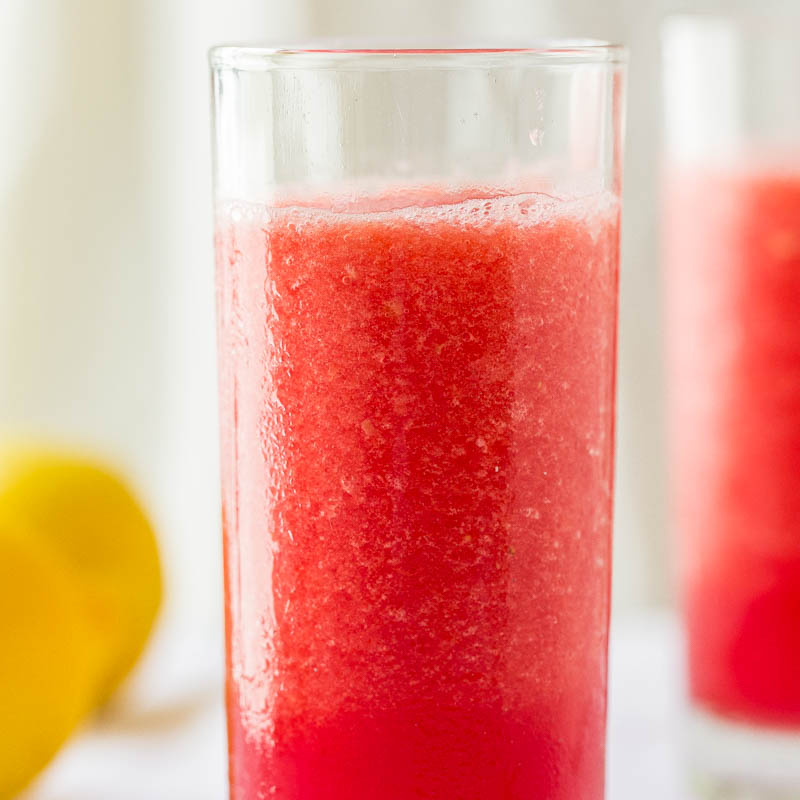 Two glasses of red slushie with a blurred background.
