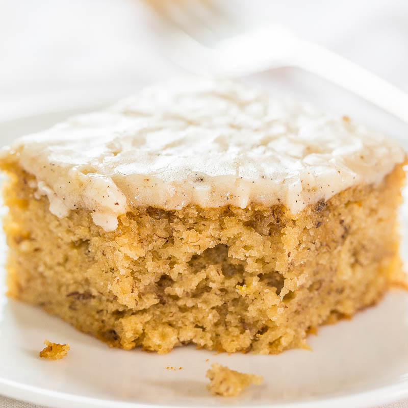A close-up of a moist slice of banana bread with a creamy frosting on top.