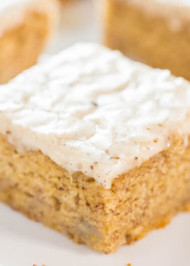 A single square piece of frosted banana cake on a plate.