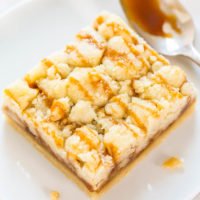 A piece of crumbly dessert topped with caramel sauce on a white plate with a spoon drizzling more sauce.