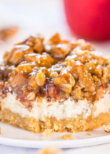 A piece of caramel walnut coffee cake on a plate with a whole red apple in the background.