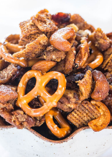 Bowl of sweet and salty snack mix with pretzels, nuts, and cereal.