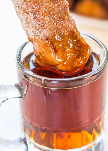 A churro being dipped into a glass mug of hot chocolate.