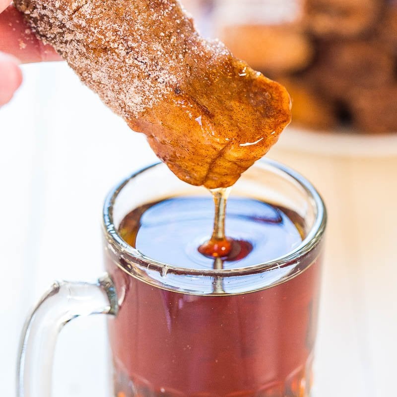 Cinnamon sugar-coated churro being dipped in a cup of hot chocolate.