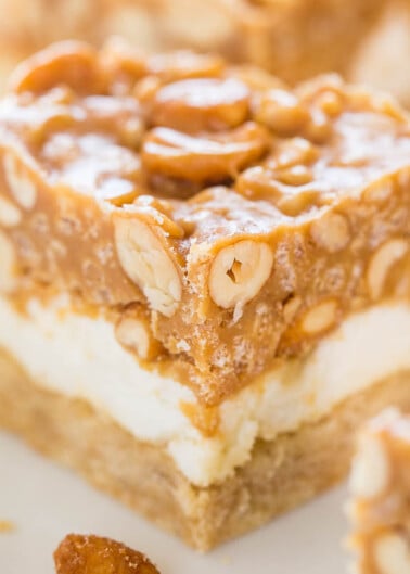 A close-up of a layered dessert bar with a nutty topping.