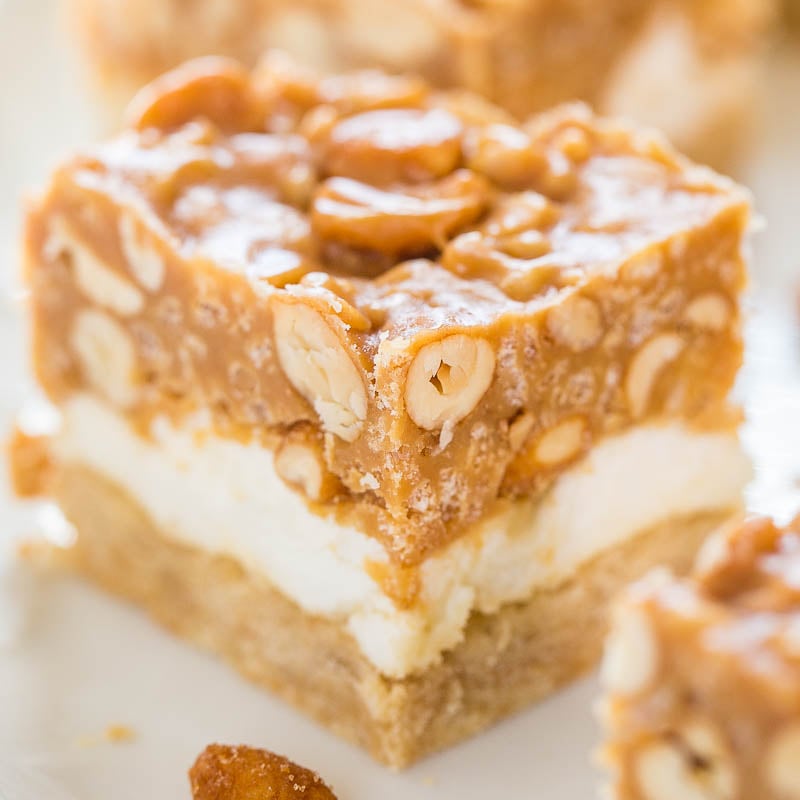 A close-up of a layered dessert bar with a nutty topping.