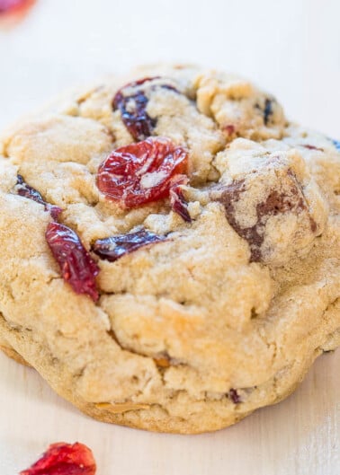 A close-up of a single chocolate chip and cranberry cookie on a light surface.