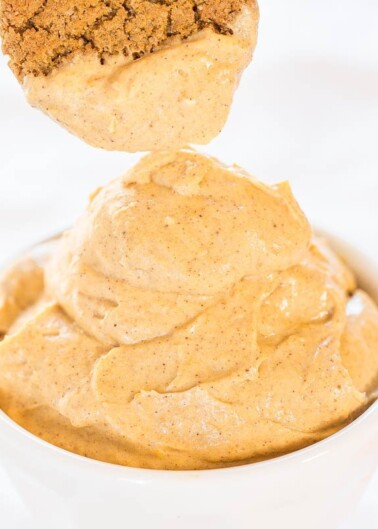 A spoonful of creamy peanut butter being lifted from a bowl, showing a smooth and spreadable texture.