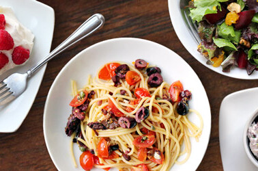 Assorted dishes on a table including pasta, salad, dessert, and a side dish.