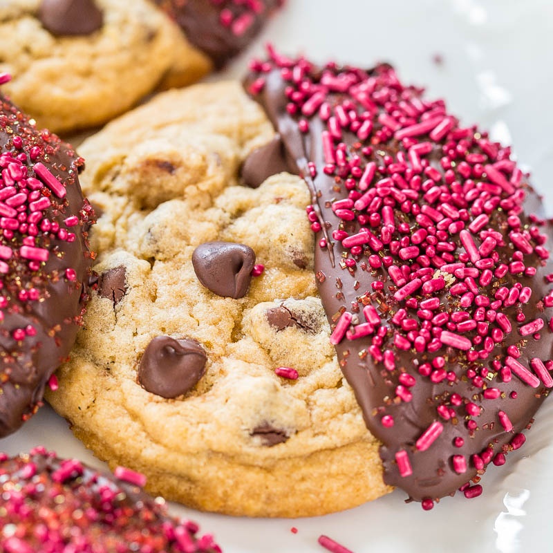 Chocolate chip cookies half-dipped in chocolate and adorned with pink sprinkles on a white plate.