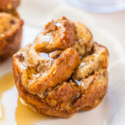 A freshly baked cinnamon roll drizzled with glaze on a white plate.